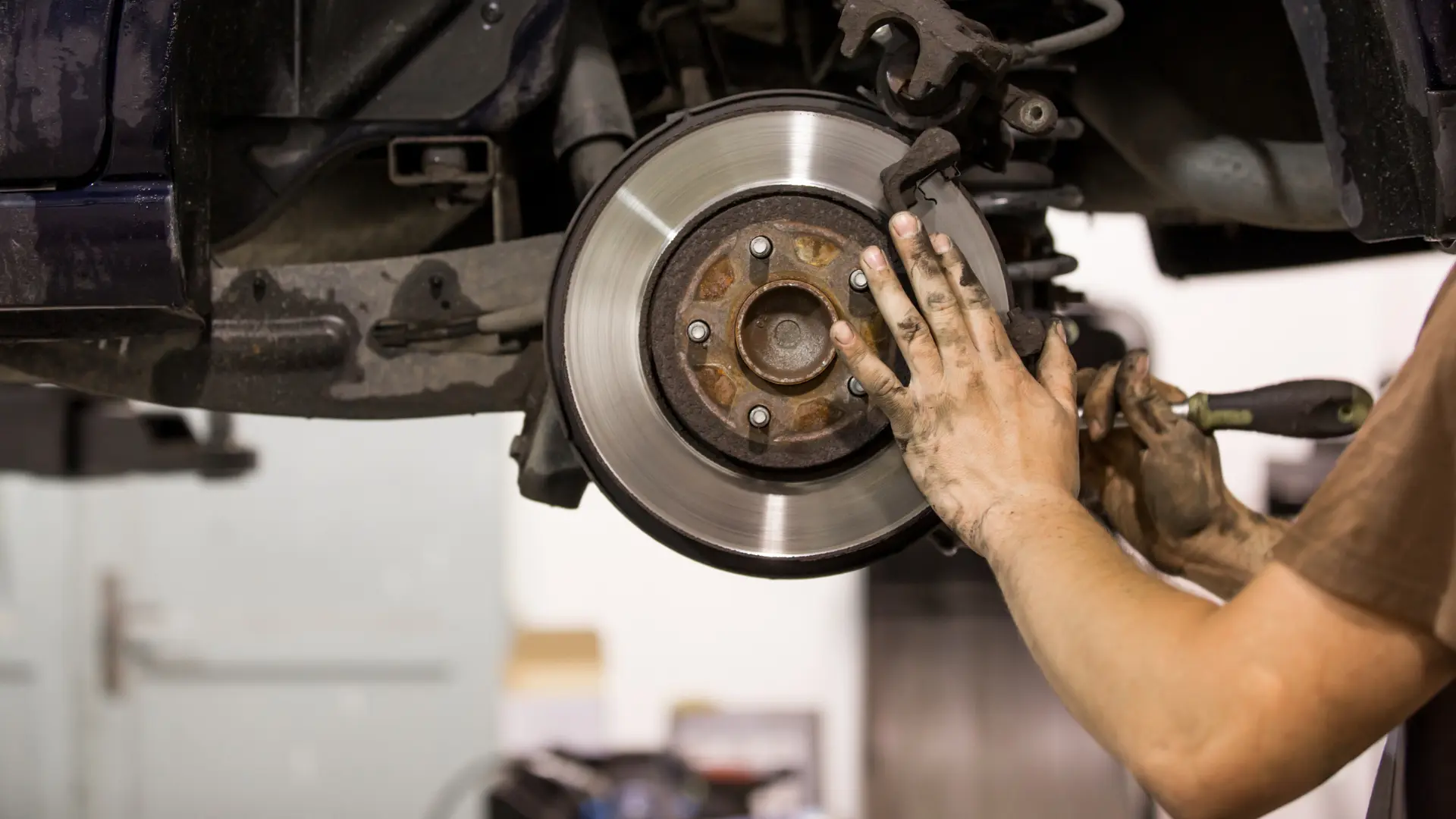 Mechanic inspecting brake disc and caliper during vehicle maintenance.